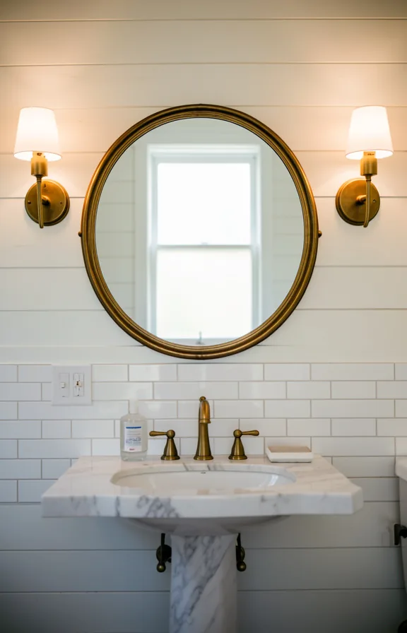 Bathroom view with vintage brass circular mirror above marble pedestal sink