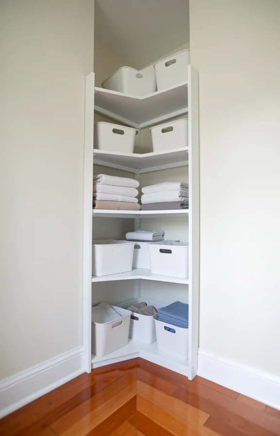 bins and folded linens neatly arranged, polished wood flooring meeting pale painted walls